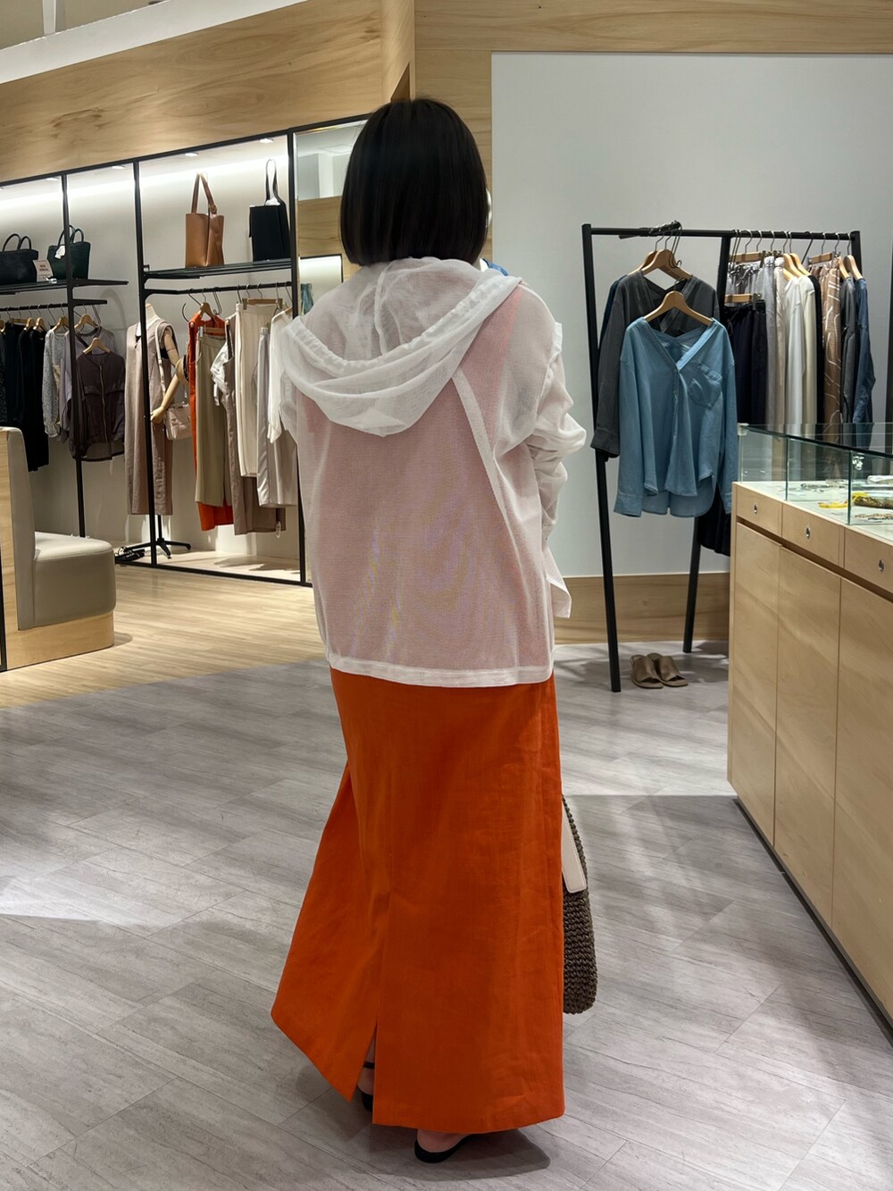 オレンジ系のワンピース、ホワイト系のパーカー、ホワイト系のトートバッグを着用したレディースの夏コーディネートの3枚目の写真