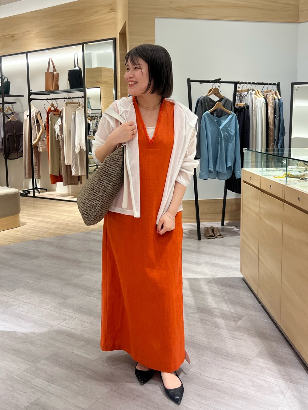 オレンジ系のワンピース、ホワイト系のパーカー、ホワイト系のトートバッグを着用したレディースの夏コーディネートの2枚目の写真