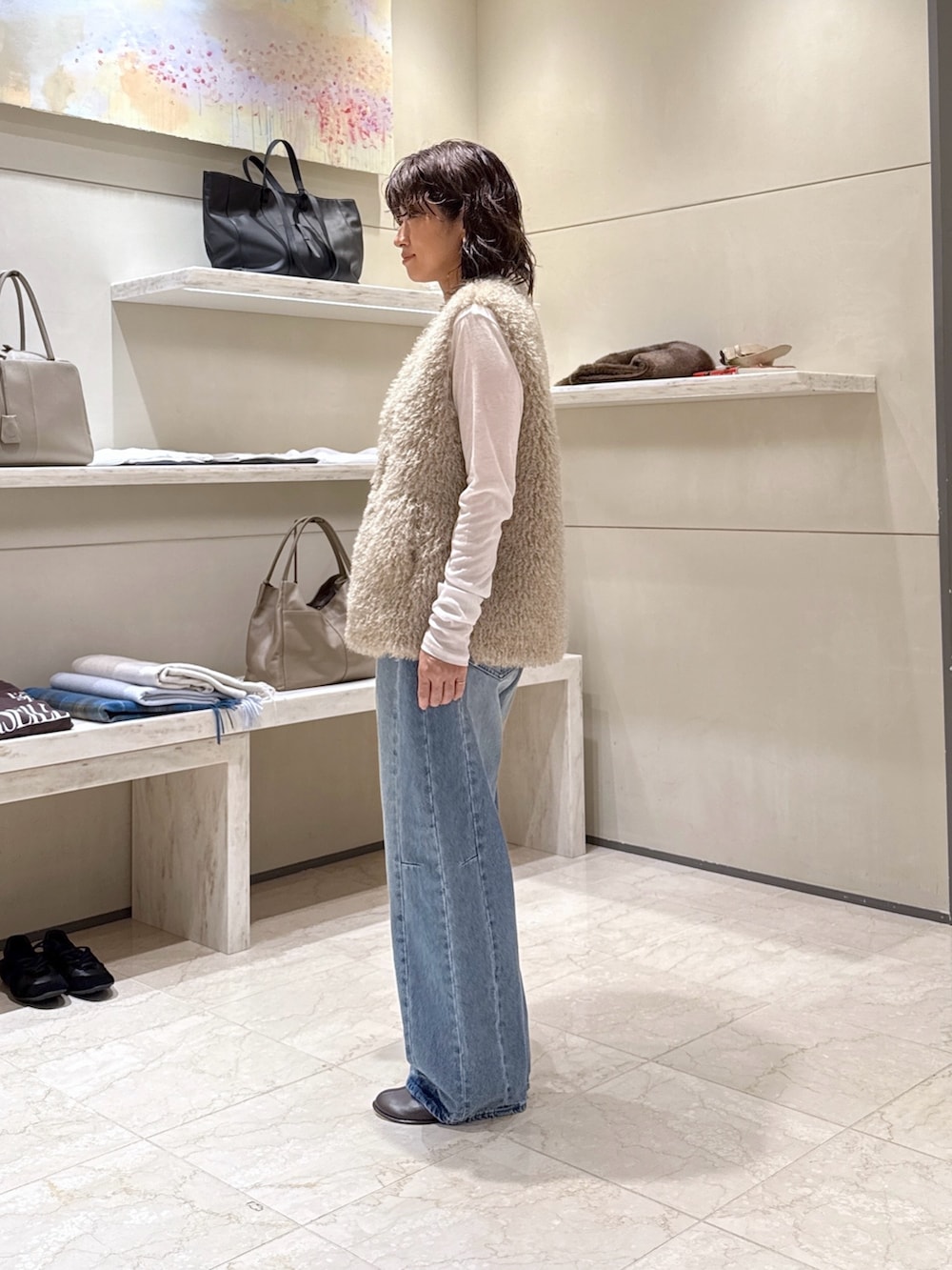 グレー系のトートバッグ、ブルー系のデニムパンツ、ベージュ系のベストを着用したレディースの秋コーディネートの2枚目の写真