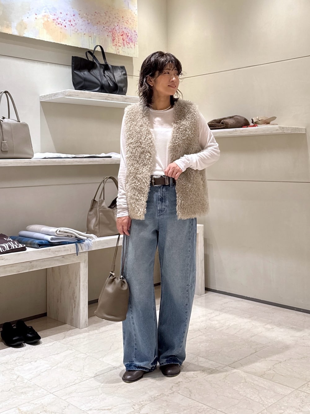 グレー系のトートバッグ、ブルー系のデニムパンツ、ベージュ系のベストを着用したレディースの秋コーディネートの4枚目の写真