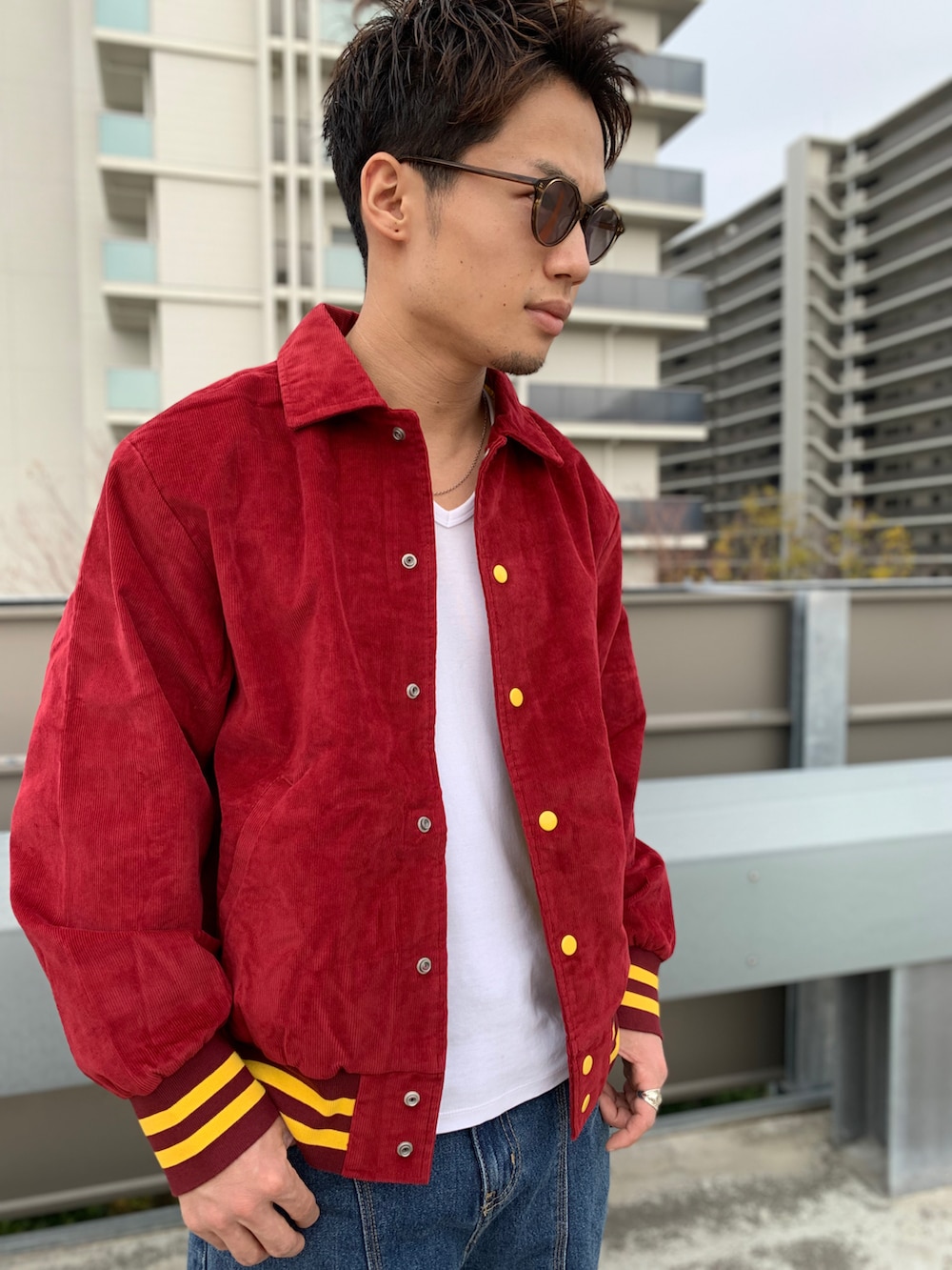 レッド系のブルゾン、ブルー系のデニムパンツ、ブラック系のブーツを着用したメンズの秋コーディネートの2枚目の写真