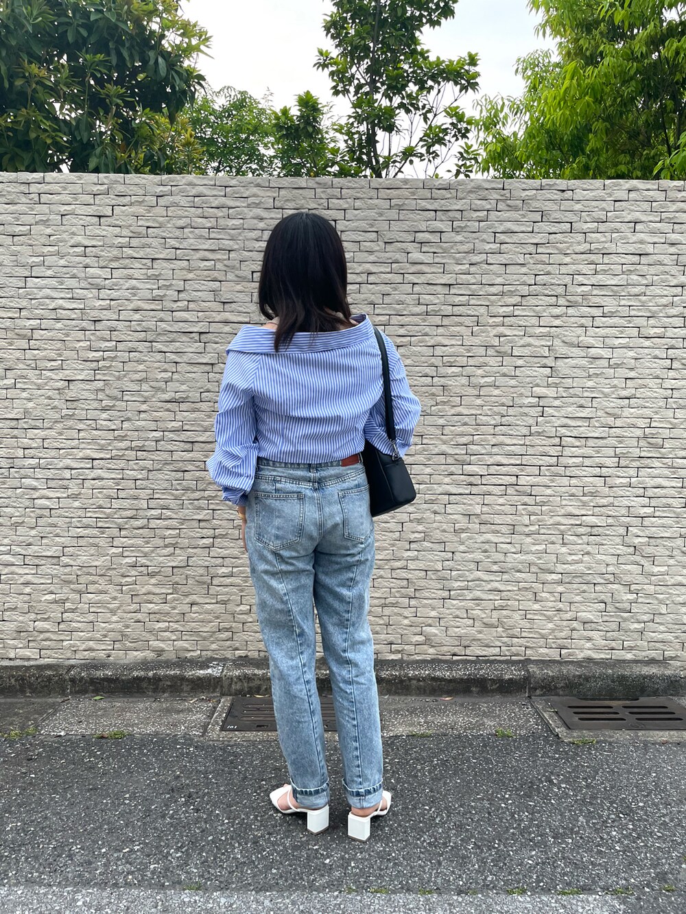 ブルー系のデニムパンツ、ブラック系のショルダーバッグ、ホワイト系のサンダルを着用したレディースの春コーディネートの2枚目の写真