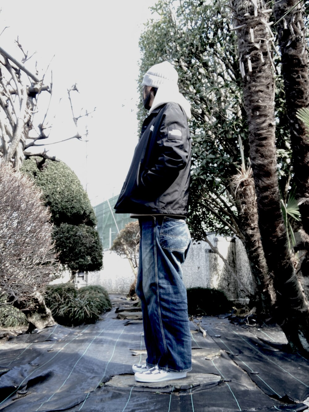 ベージュ系のパーカー、ブラック系のナイロンジャケット、ブルー系のデニムパンツを着用したメンズの春コーディネートの3枚目の写真