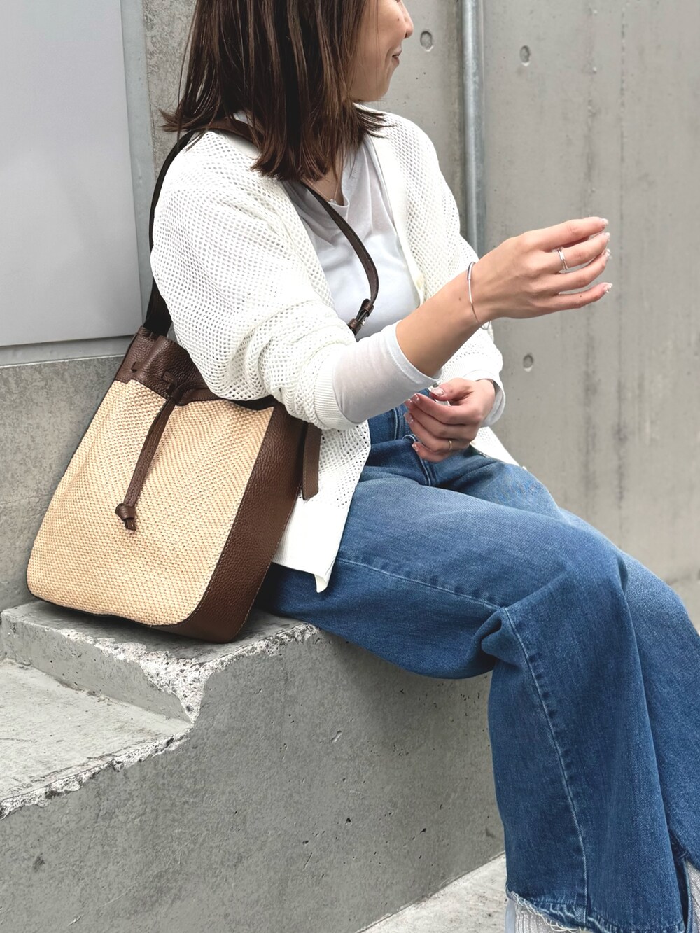 ブルー系のデニムパンツ、ブラウン系のショルダーバッグ、ホワイト系のカーディガン/ボレロを着用したレディースの春コーディネートの6枚目の写真