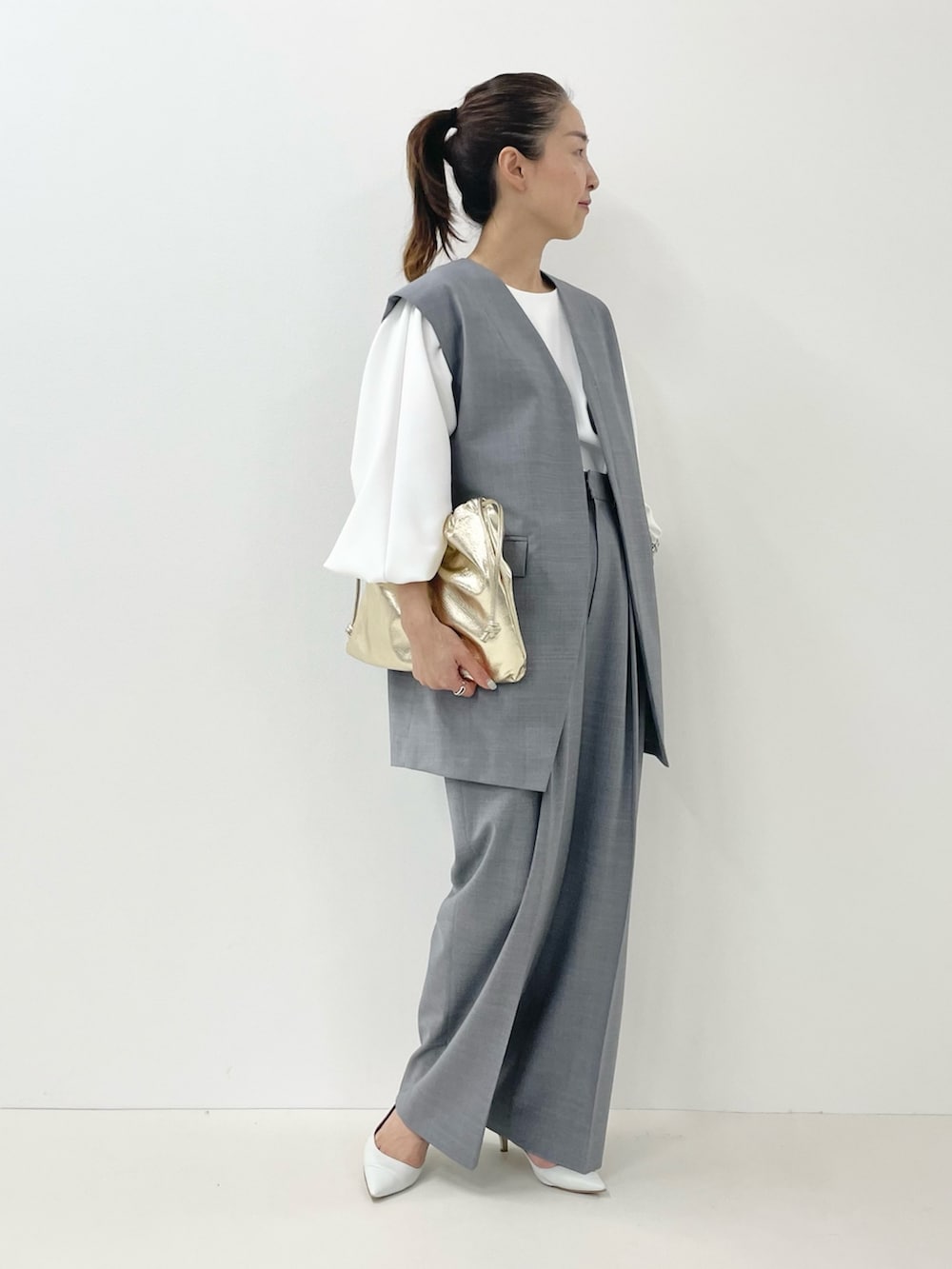 ゴールド系のショルダーバッグ、ホワイト系のTシャツ/カットソー、グレー系のベストを着用したレディースの冬コーディネートの3枚目の写真