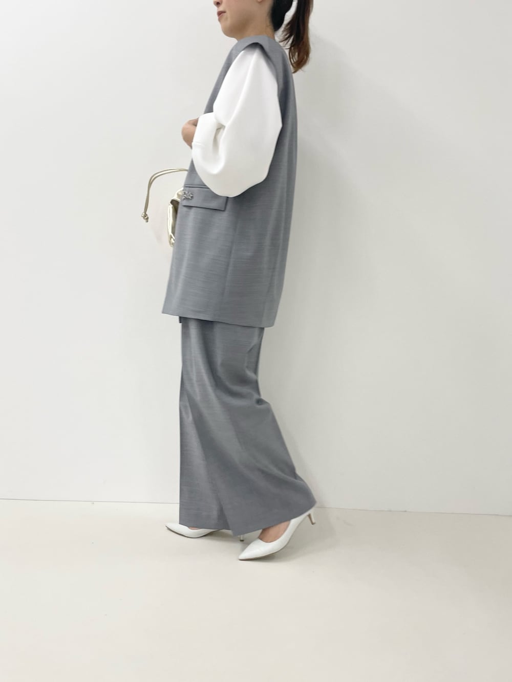 ゴールド系のショルダーバッグ、ホワイト系のTシャツ/カットソー、グレー系のベストを着用したレディースの冬コーディネートの9枚目の写真