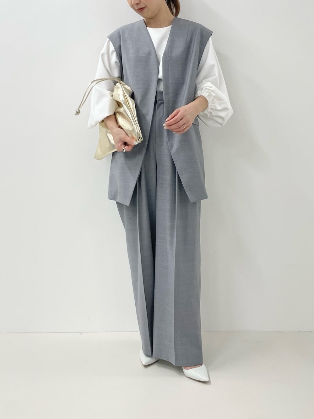 ゴールド系のショルダーバッグ、ホワイト系のTシャツ/カットソー、グレー系のベストを着用したレディースの冬コーディネートの2枚目の写真