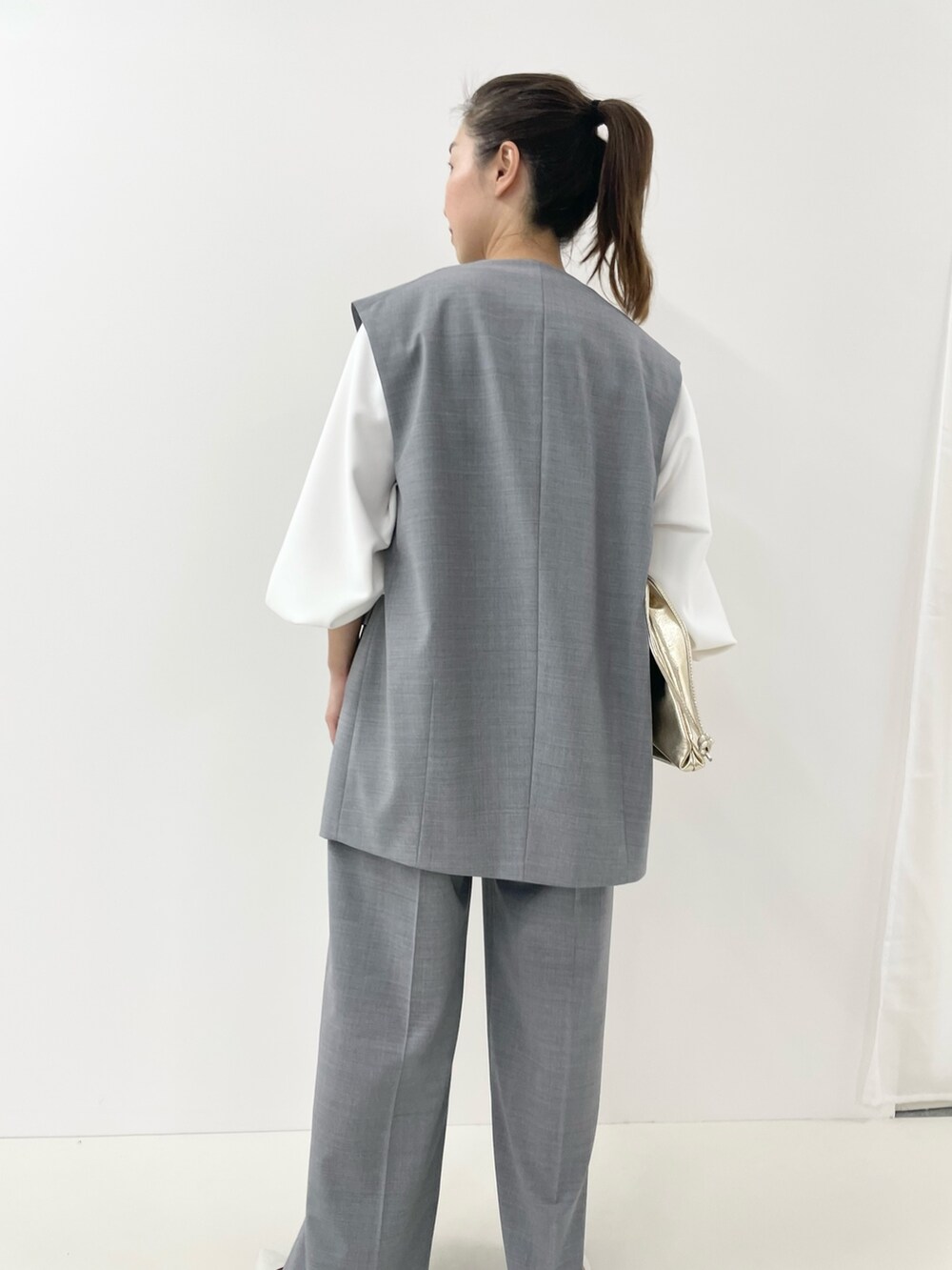 ゴールド系のショルダーバッグ、ホワイト系のTシャツ/カットソー、グレー系のベストを着用したレディースの冬コーディネートの6枚目の写真