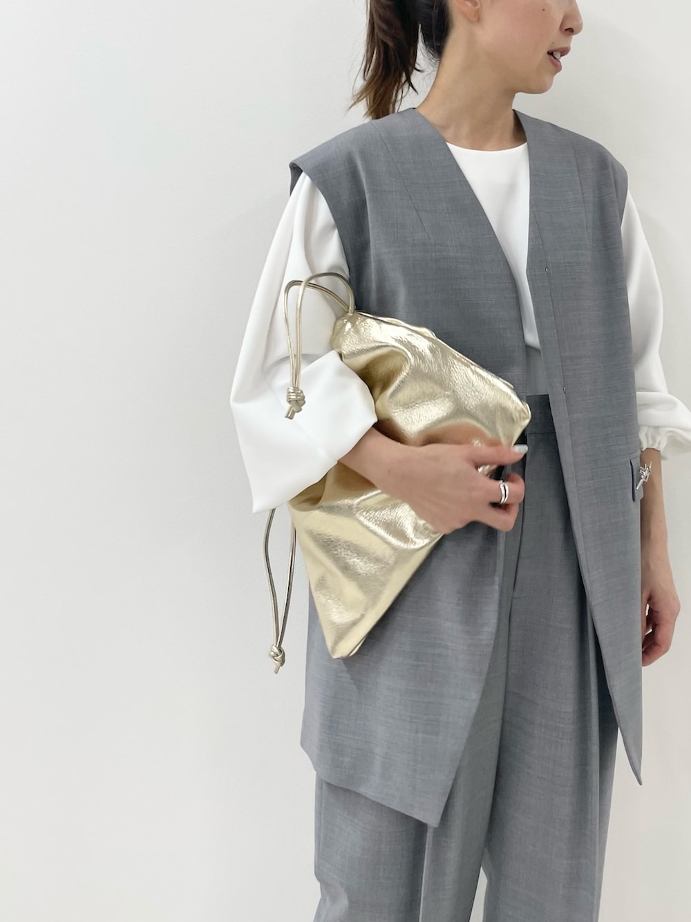 ゴールド系のショルダーバッグ、ホワイト系のTシャツ/カットソー、グレー系のベストを着用したレディースの冬コーディネートの5枚目の写真