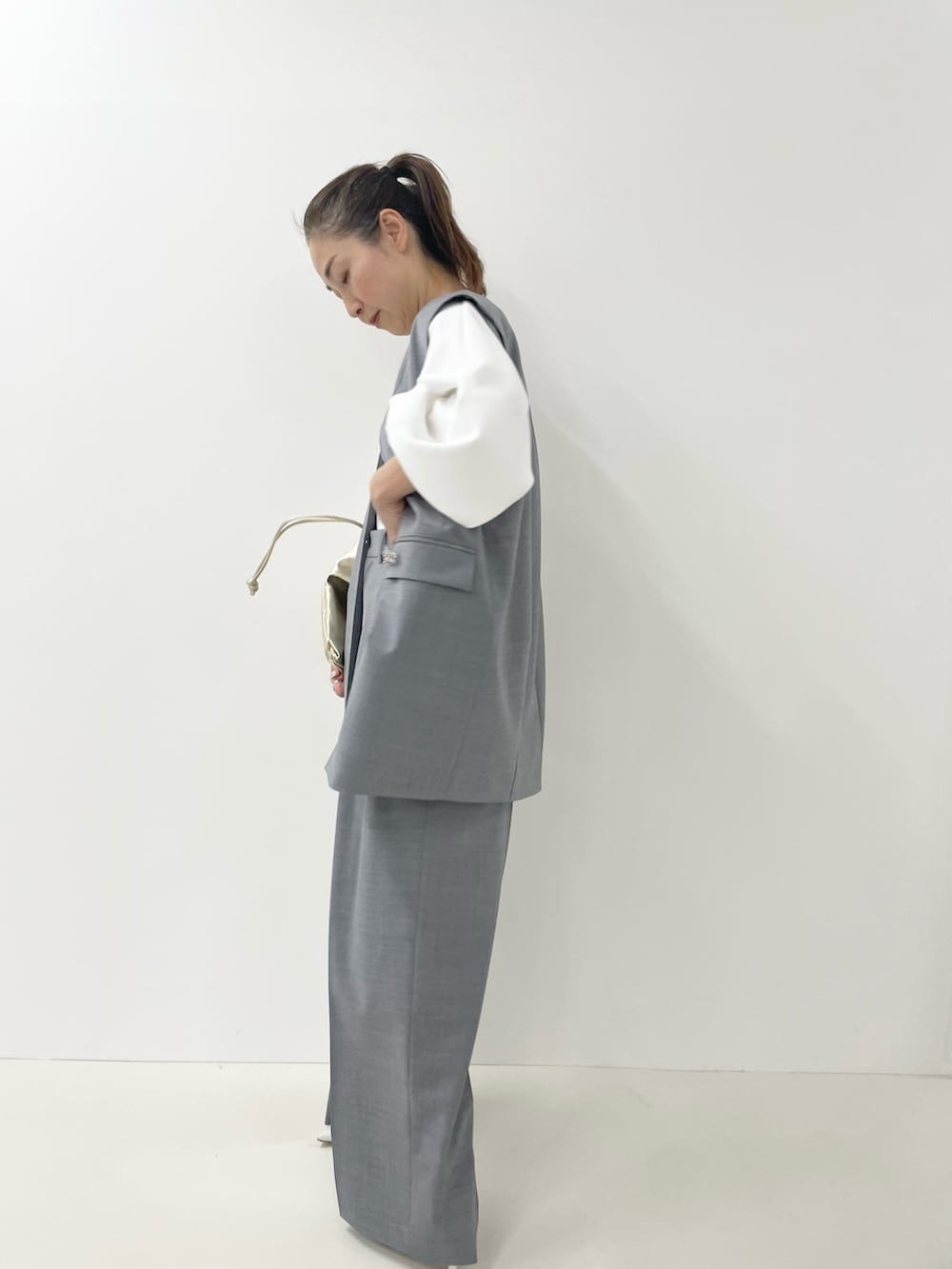 ゴールド系のショルダーバッグ、ホワイト系のTシャツ/カットソー、グレー系のベストを着用したレディースの冬コーディネートの7枚目の写真