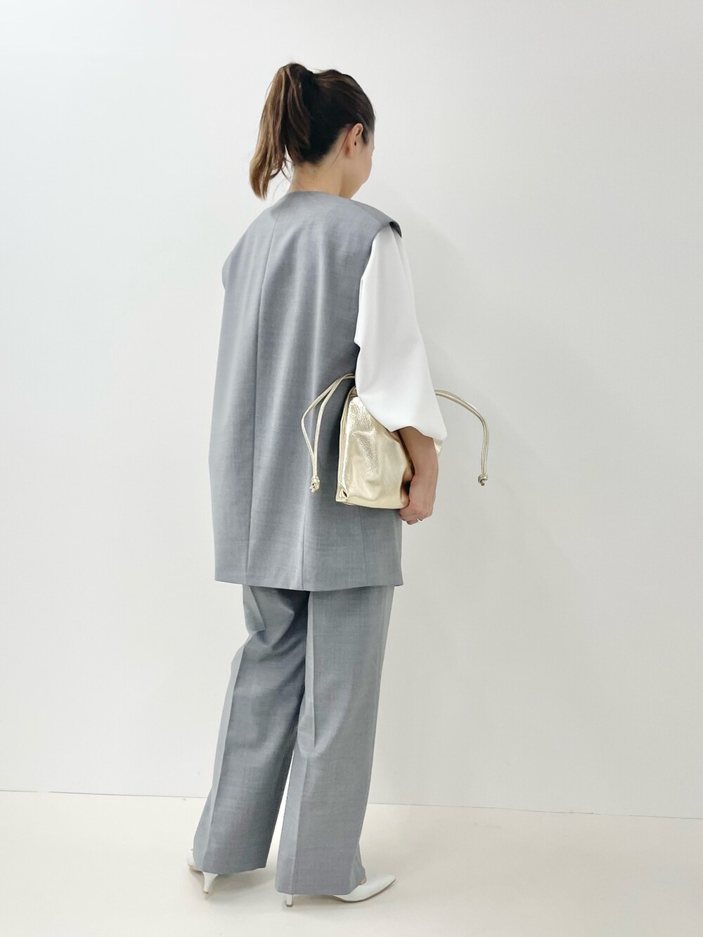 ゴールド系のショルダーバッグ、ホワイト系のTシャツ/カットソー、グレー系のベストを着用したレディースの冬コーディネートの4枚目の写真