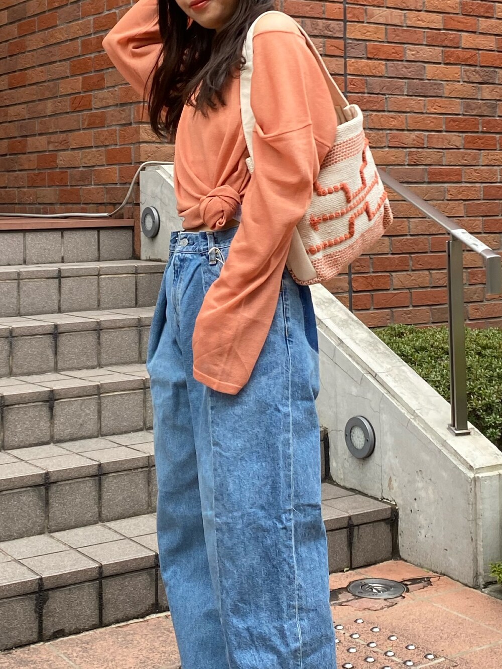 オレンジ系のニット/セーター、ブルー系のデニムパンツ、ブラック系のサンダルを着用したレディースの春コーディネートの7枚目の写真