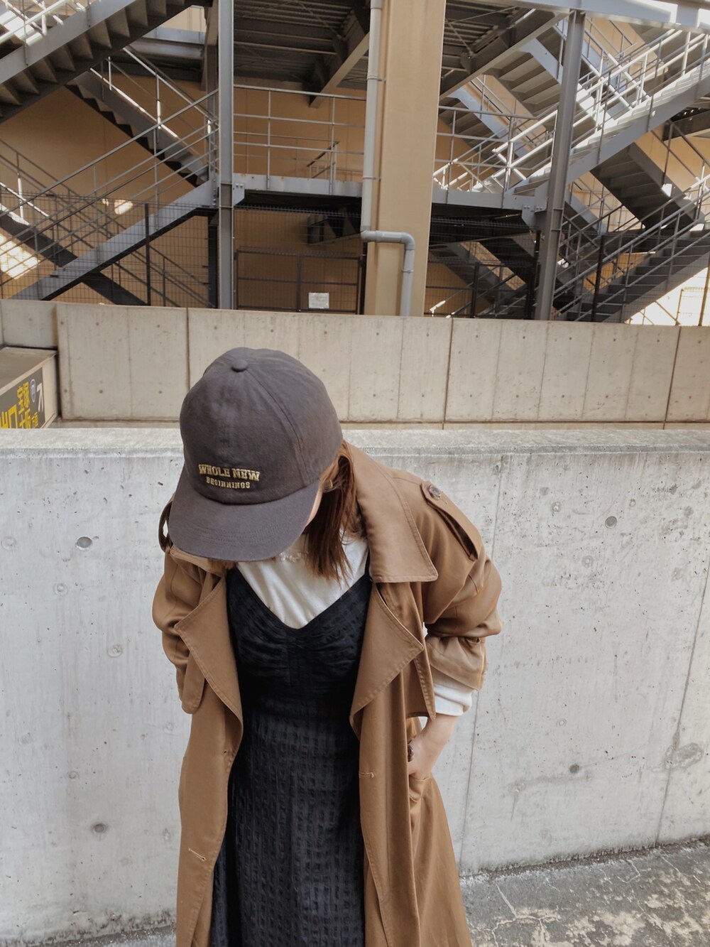 イエロー系のトレンチコート、ブラック系のワンピース、グレー系のキャップを着用したレディースの春コーディネートの4枚目の写真