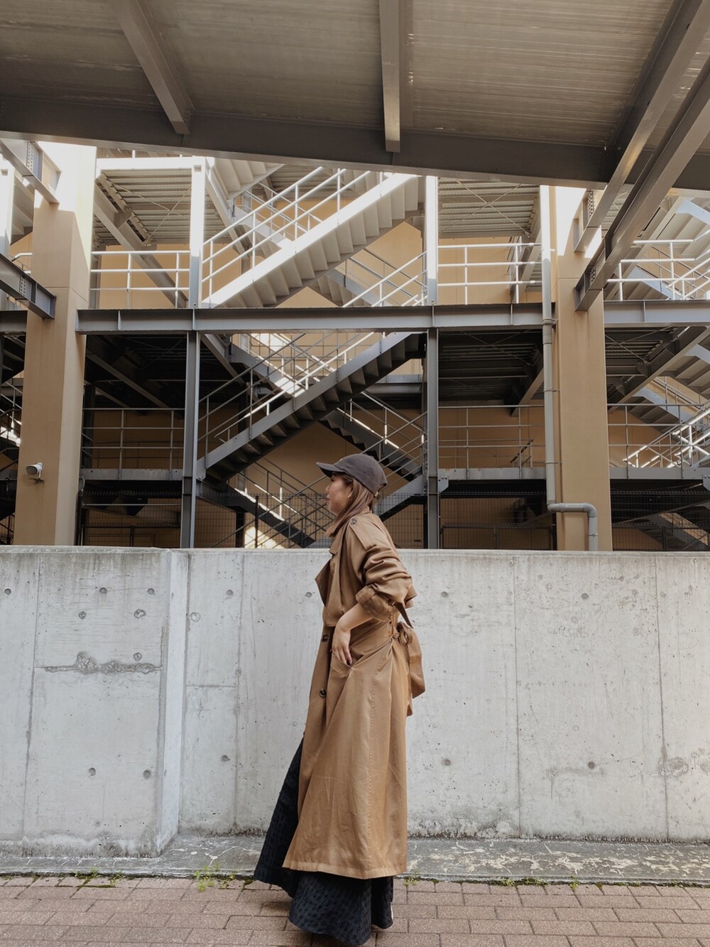 イエロー系のトレンチコート、ブラック系のワンピース、グレー系のキャップを着用したレディースの春コーディネートの5枚目の写真