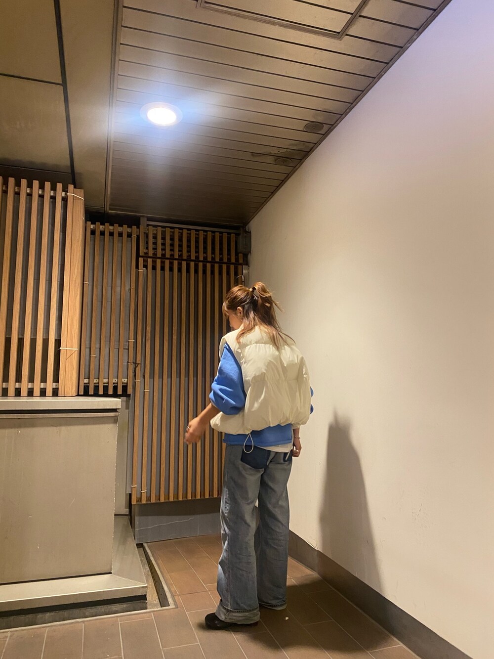 ホワイト系のダウンベスト、ブルー系のニット/セーター、ブルー系のデニムパンツを着用したレディースの秋コーディネートの3枚目の写真