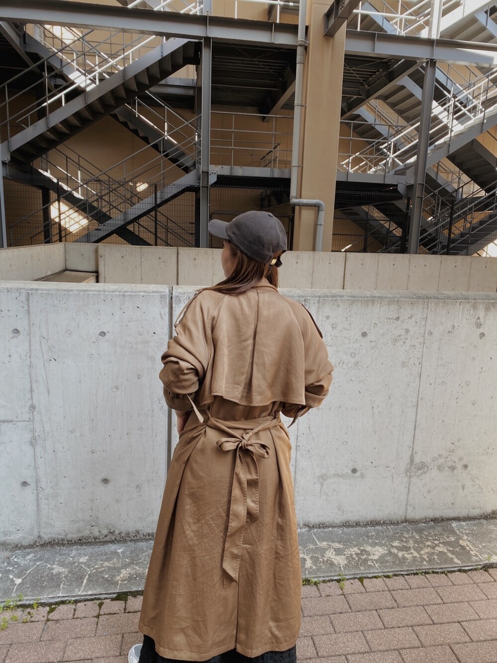 イエロー系のトレンチコート、ブラック系のワンピース、グレー系のキャップを着用したレディースの春コーディネートの3枚目の写真