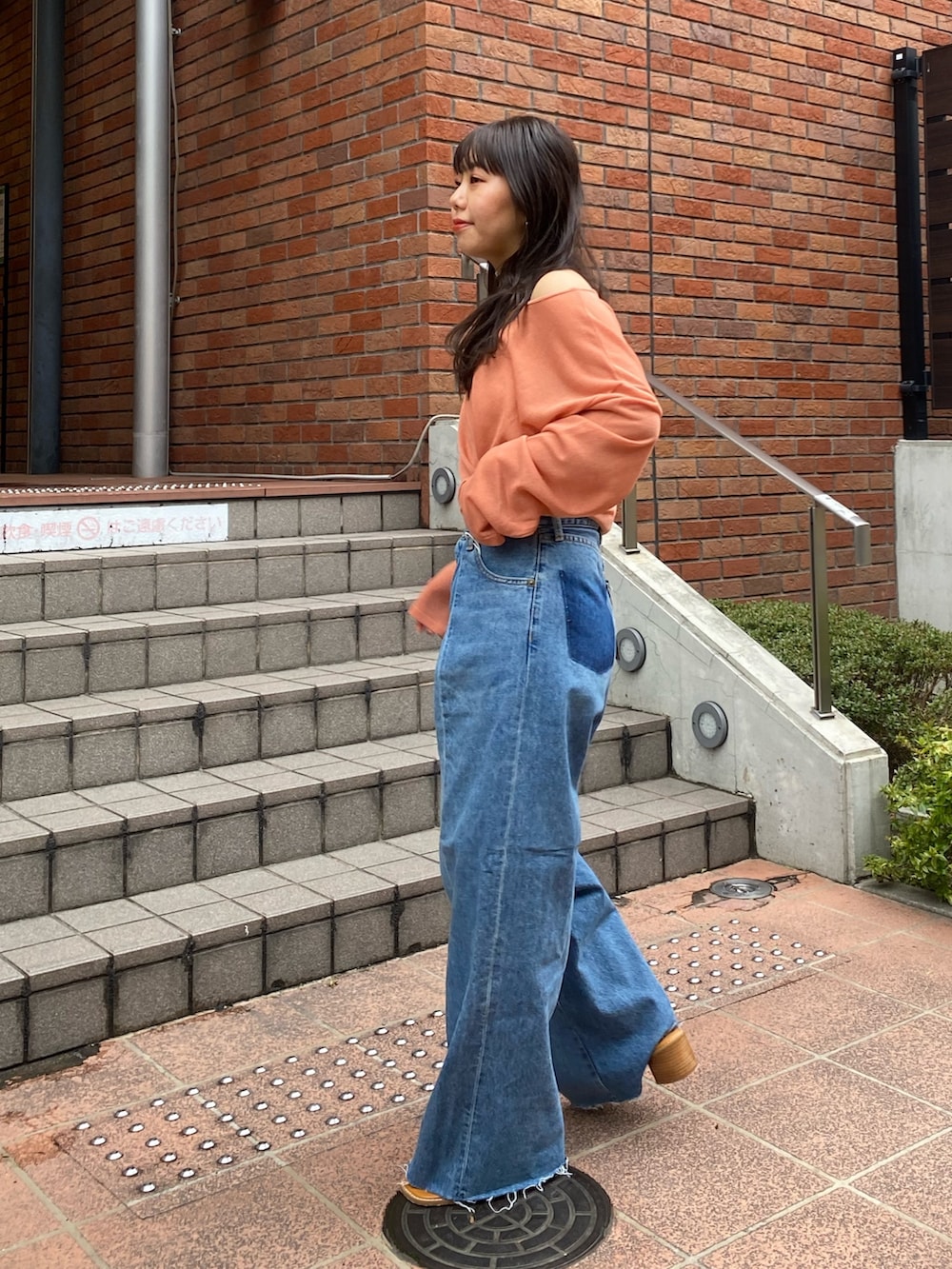 オレンジ系のニット/セーター、ブルー系のデニムパンツ、ブラック系のサンダルを着用したレディースの春コーディネートの2枚目の写真