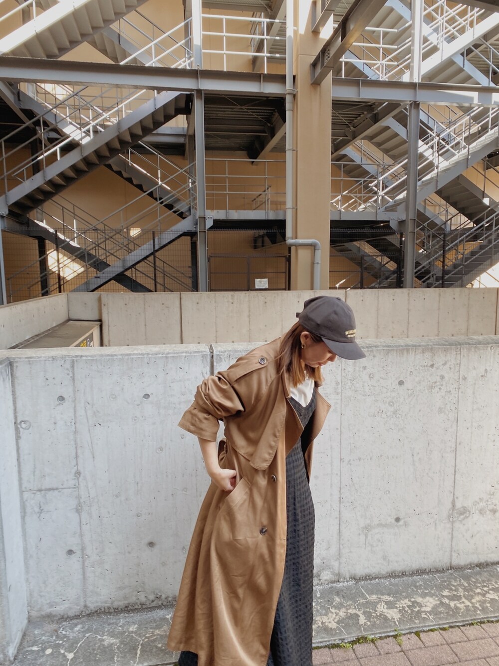 イエロー系のトレンチコート、ブラック系のワンピース、グレー系のキャップを着用したレディースの春コーディネートの2枚目の写真