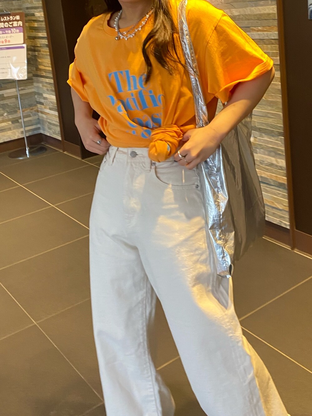 オレンジ系のTシャツ/カットソー、ホワイト系のデニムパンツを着用したレディースの春コーディネートの6枚目の写真