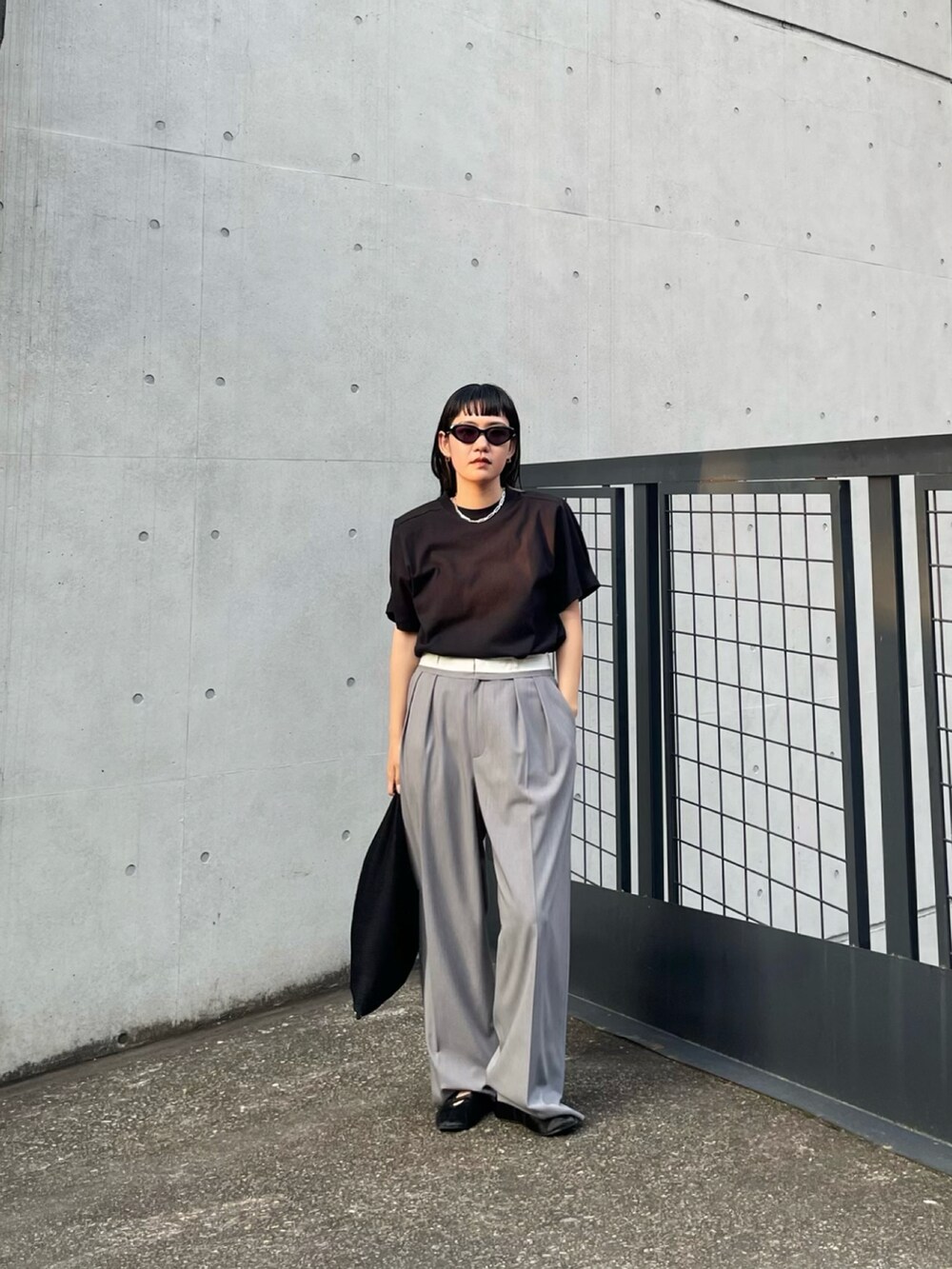 ブラック系のTシャツ/カットソー、グレー系のスラックス、ブラック系のトートバッグを着用したレディースの夏コーディネートの2枚目の写真