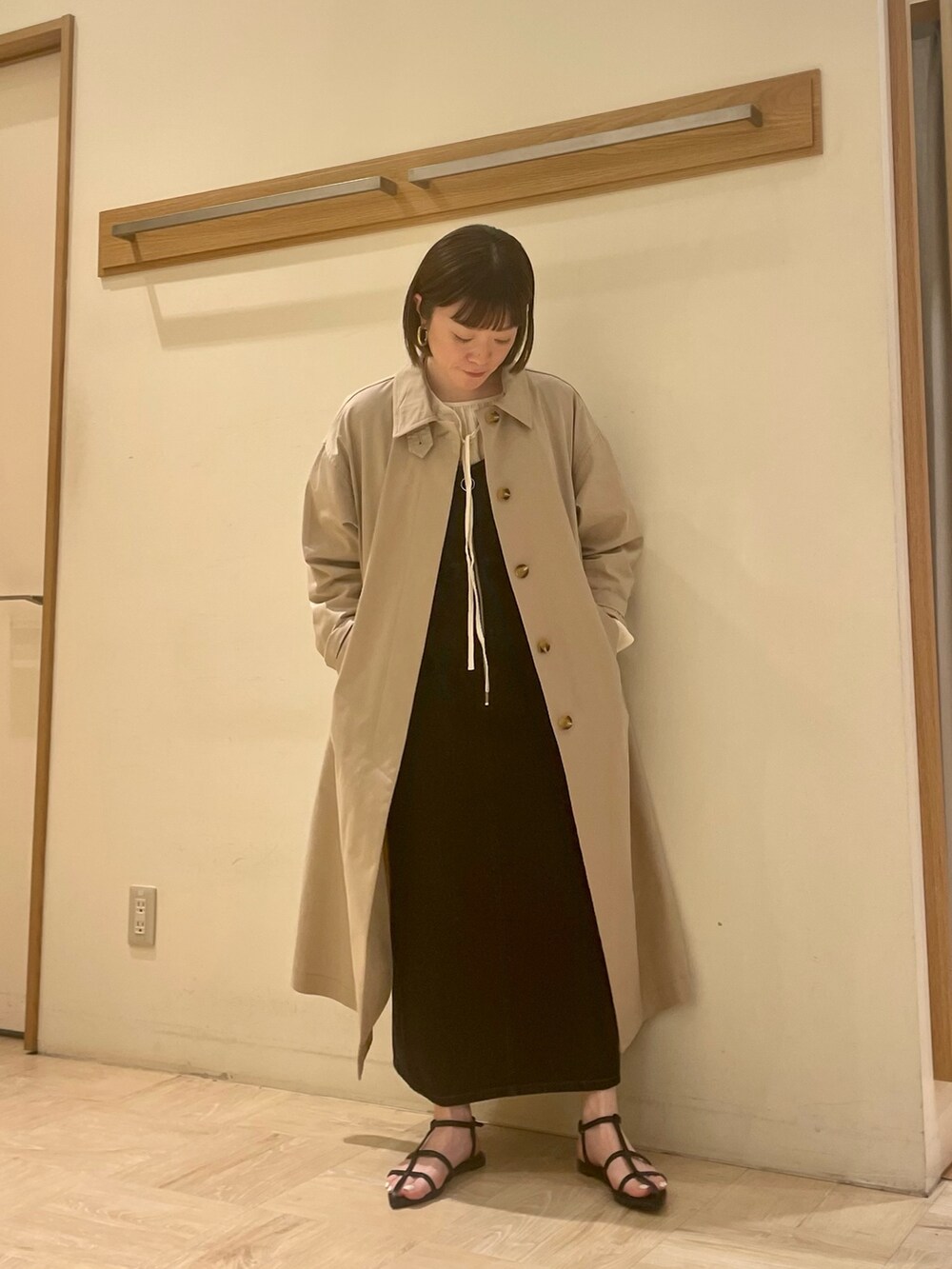 ベージュ系のステンカラーコート、ブラック系のジャンパースカート、ホワイト系のシャツ/ブラウスを着用したレディースの春コーディネートの4枚目の写真