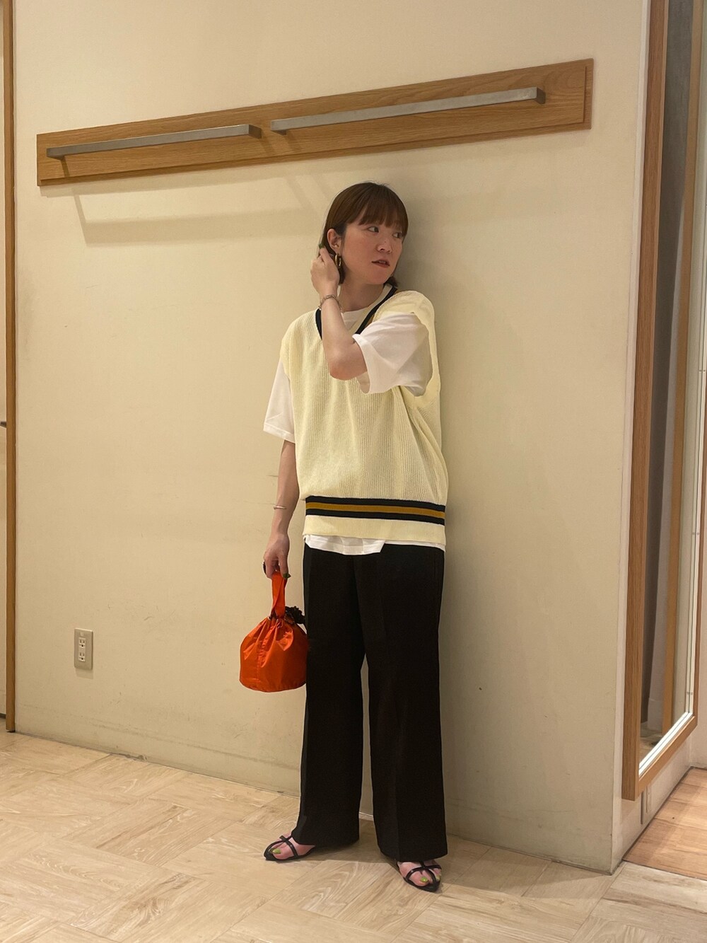 ブラック系のスラックス、ブラック系のサンダル、オレンジ系のショルダーバッグを着用したレディースの夏コーディネートの2枚目の写真