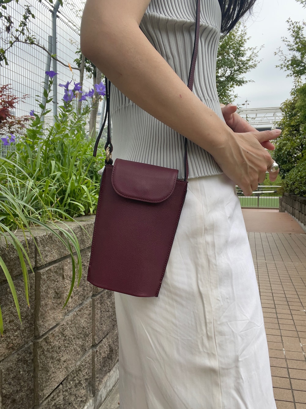 グレー系のトップス、レッド系のショルダーバッグ、ホワイト系のパンツを着用したレディースの夏コーディネートの2枚目の写真