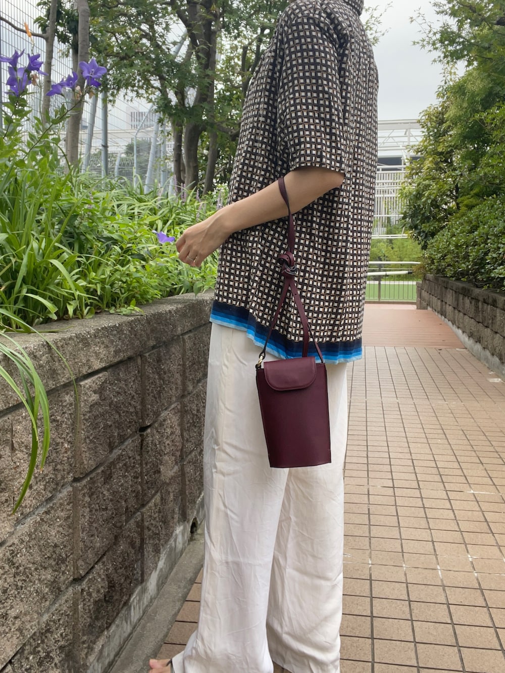 グレー系のトップス、レッド系のショルダーバッグ、ホワイト系のパンツを着用したレディースの夏コーディネートの3枚目の写真