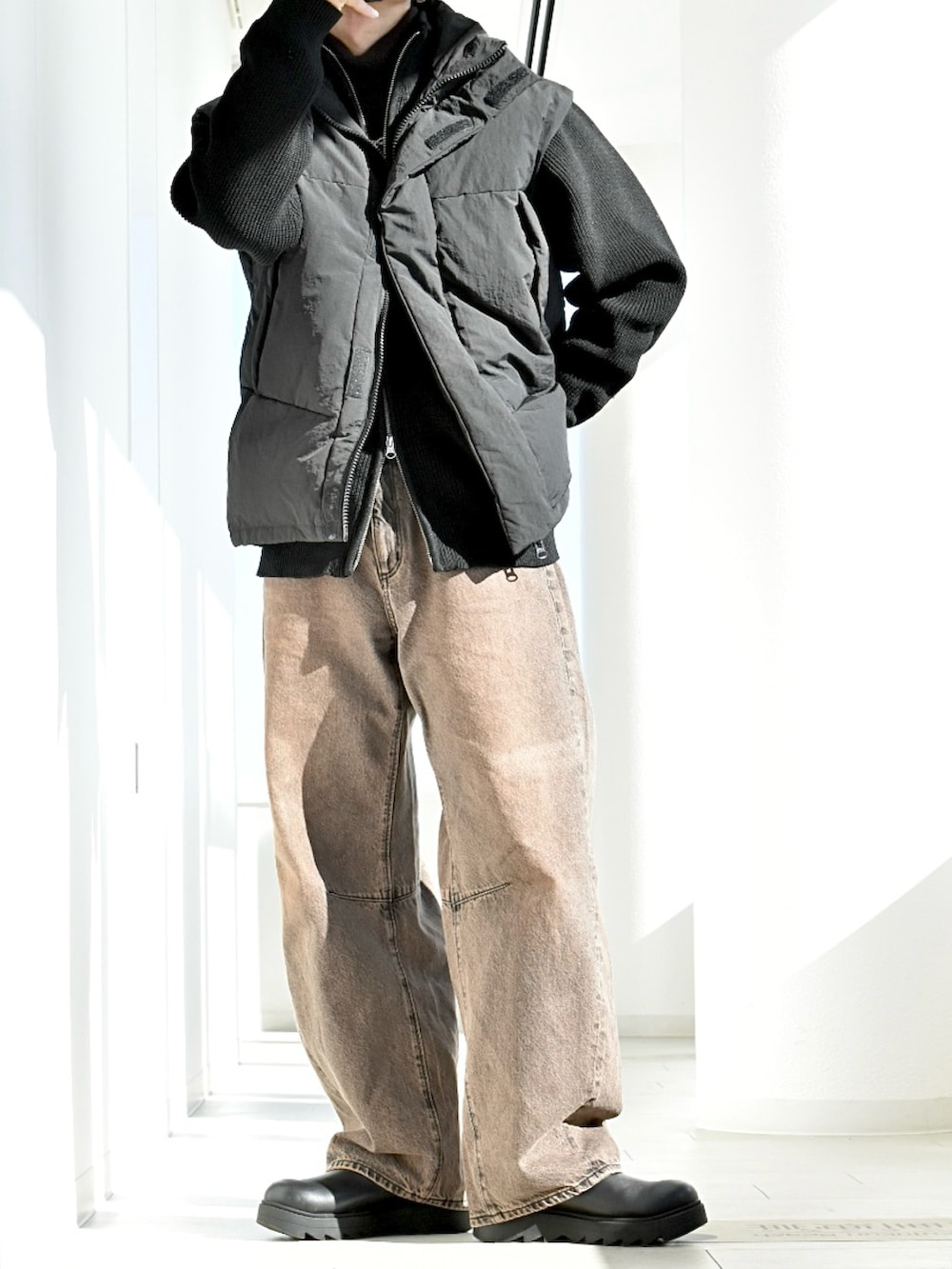 ブラック系のダウンベスト、ブラック系のニット/セーター、ブラウン系のデニムパンツを着用したメンズの冬コーディネートの2枚目の写真