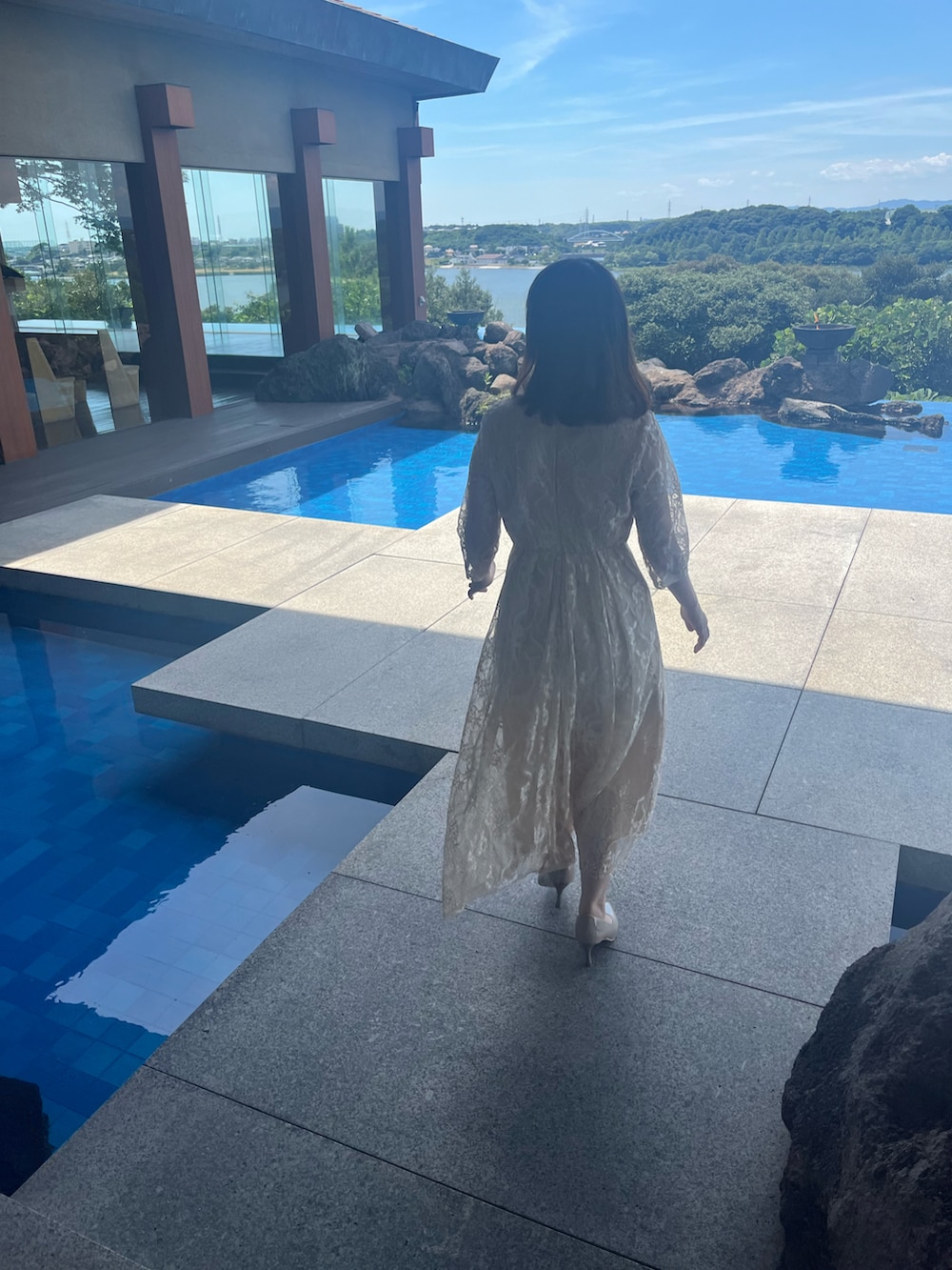 ホワイト系のショルダーバッグ、ベージュ系のドレス、グレー系のパンプスを着用したレディースの夏コーディネートの2枚目の写真