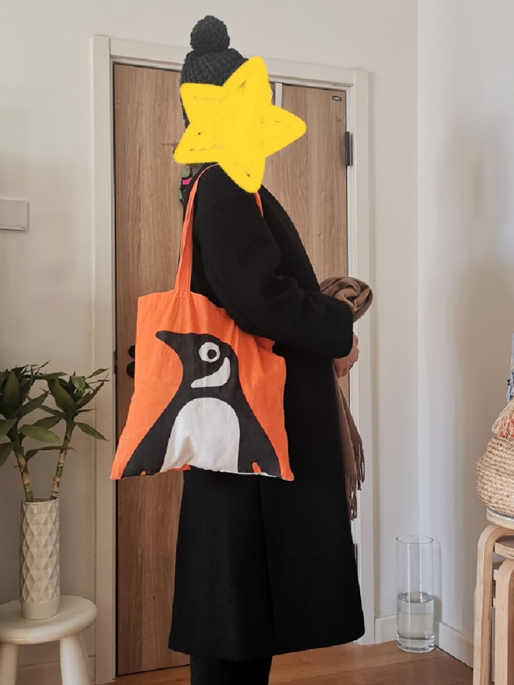 ブラック系のノーカラーコート、ブラック系のチノパンツ、オレンジ系のエコバッグ/サブバッグを着用したレディースの冬コーディネートの3枚目の写真