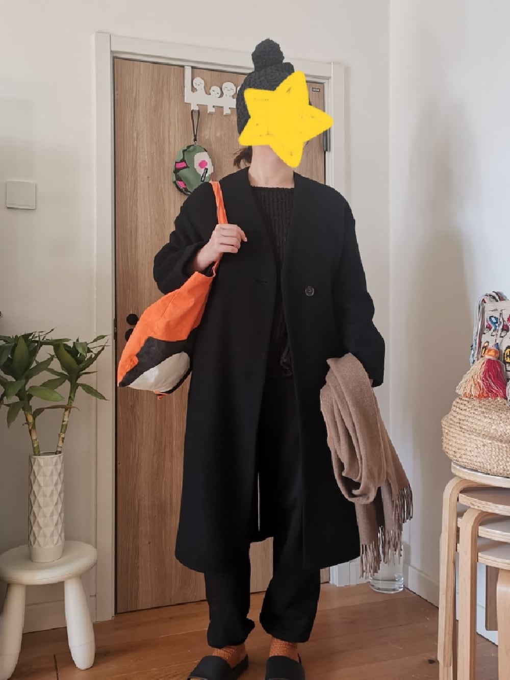 ブラック系のノーカラーコート、ブラック系のチノパンツ、オレンジ系のエコバッグ/サブバッグを着用したレディースの冬コーディネートの2枚目の写真