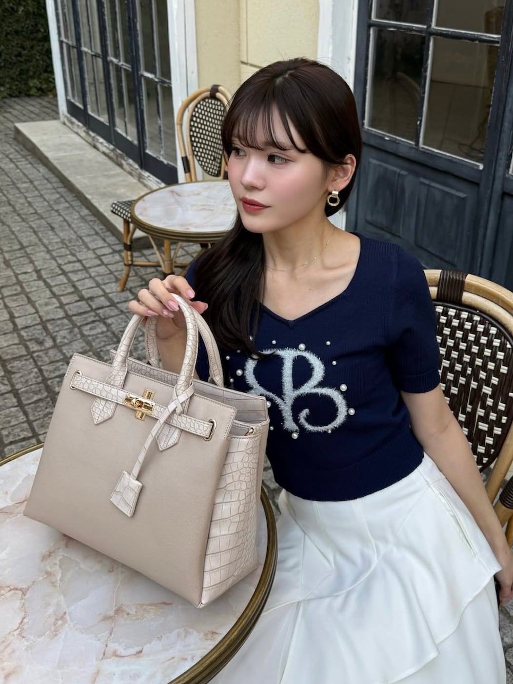 ホワイト系のスカート、ブルー系のニット/セーター、ベージュ系のショルダーバッグを着用したレディースの春コーディネートの2枚目の写真