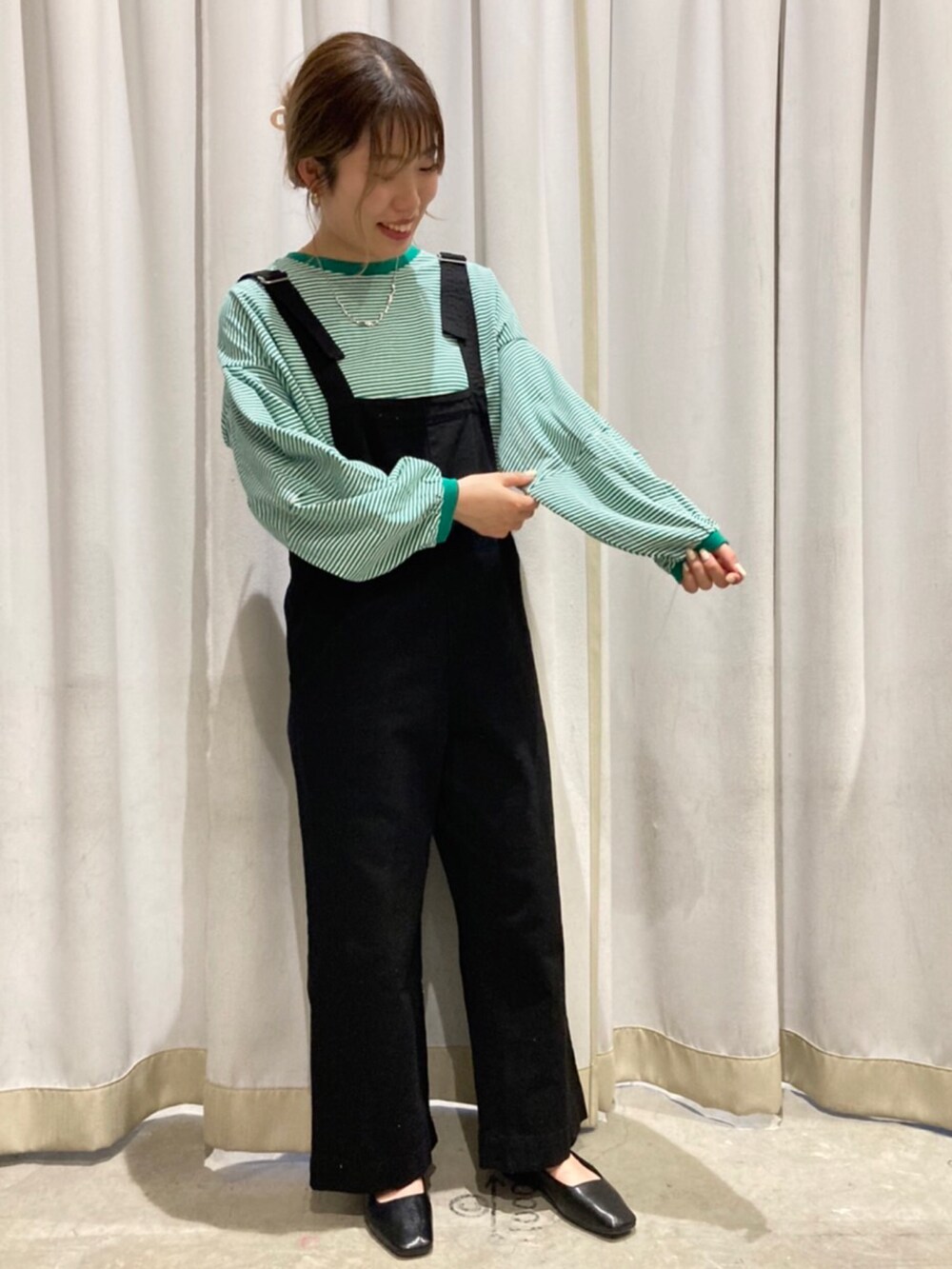 ブラック系のサロペット/オーバーオール、ブラック系のパンプス、グリーン系のTシャツ/カットソーを着用したレディースの冬コーディネートの2枚目の写真