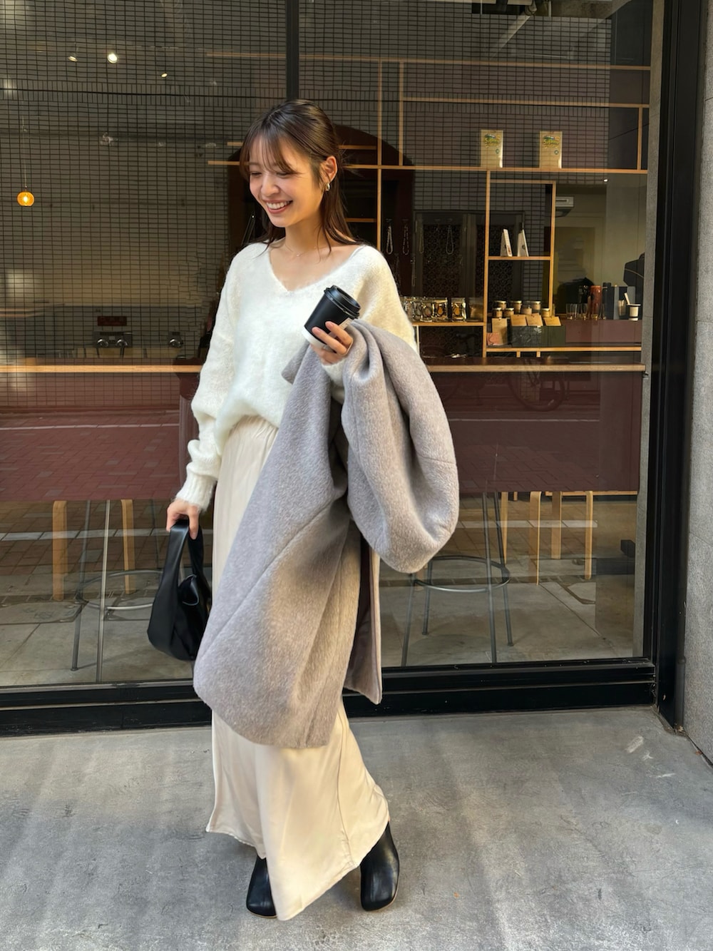 グレー系のノーカラーコート、ベージュ系のスカートを着用したレディースの冬コーディネートの2枚目の写真