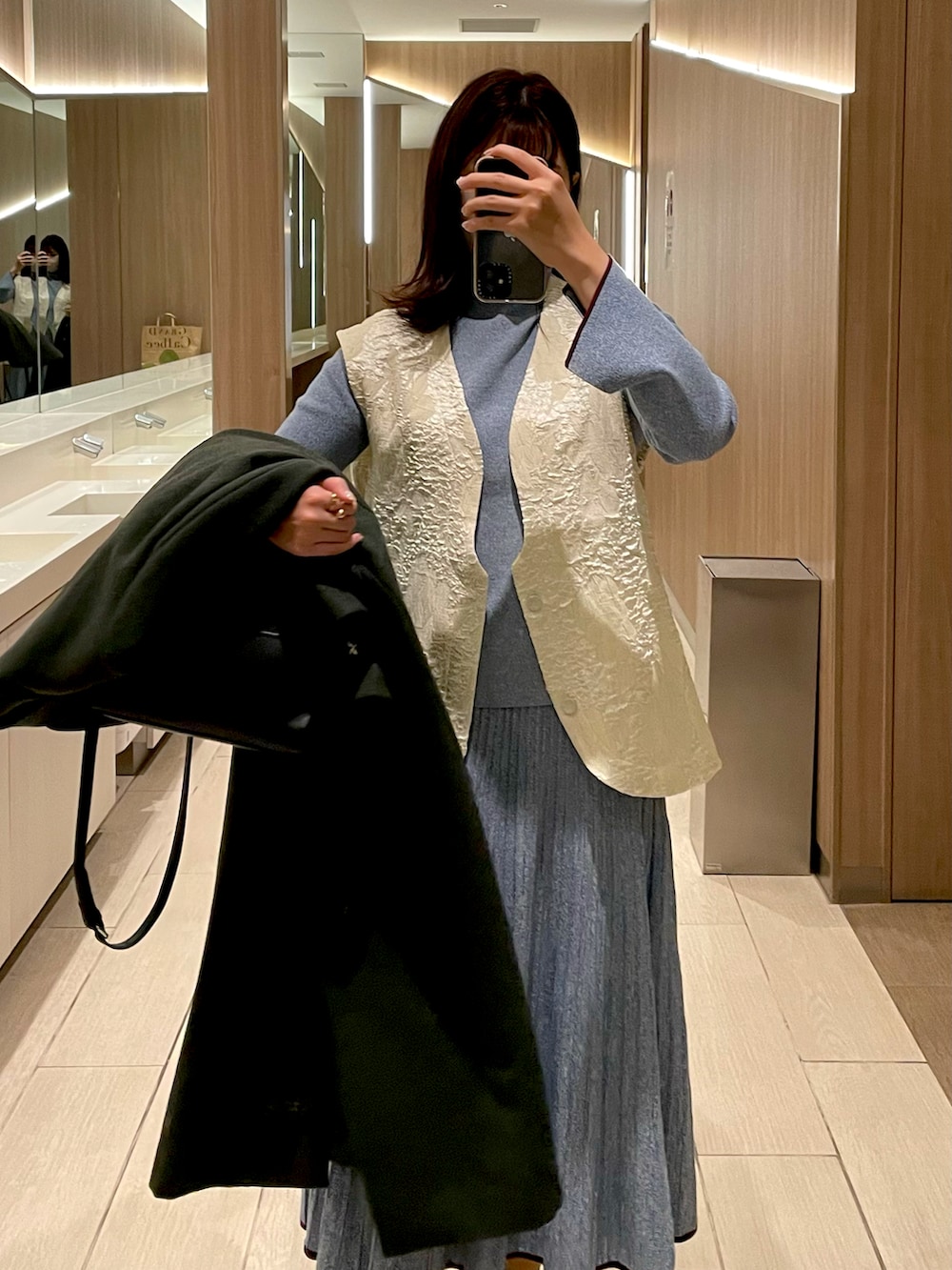 ブラック系のボストンバッグ、グリーン系のチェスターコート、ホワイト系のベストを着用したレディースの冬コーディネートの2枚目の写真