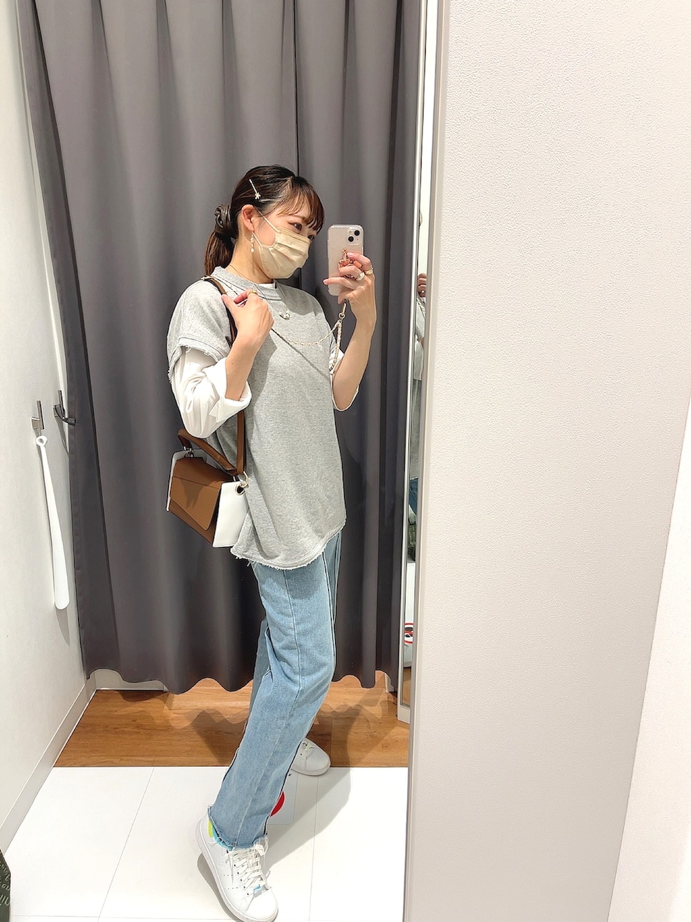 ブラウン系のハンドバッグ、ブルー系のデニムパンツ、ホワイト系のスニーカーを着用したレディースの春コーディネートの2枚目の写真