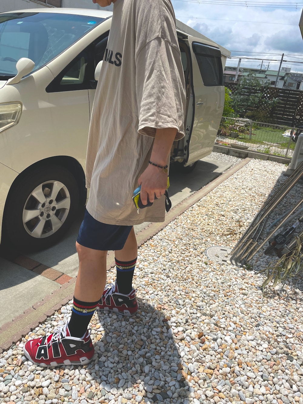 ベージュ系のTシャツ/カットソー、ブラック系のパンツ、レッド系のスニーカーを着用したメンズの夏コーディネートの2枚目の写真