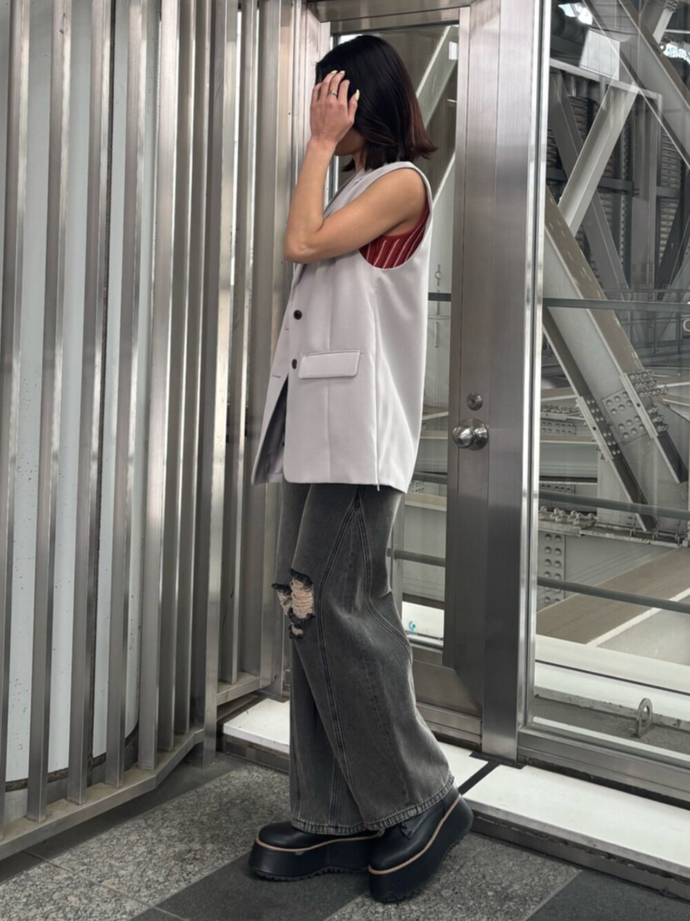 ベージュ系のベスト、オレンジ系のニット/セーター、グレー系のデニムパンツを着用したレディースの春コーディネートの2枚目の写真