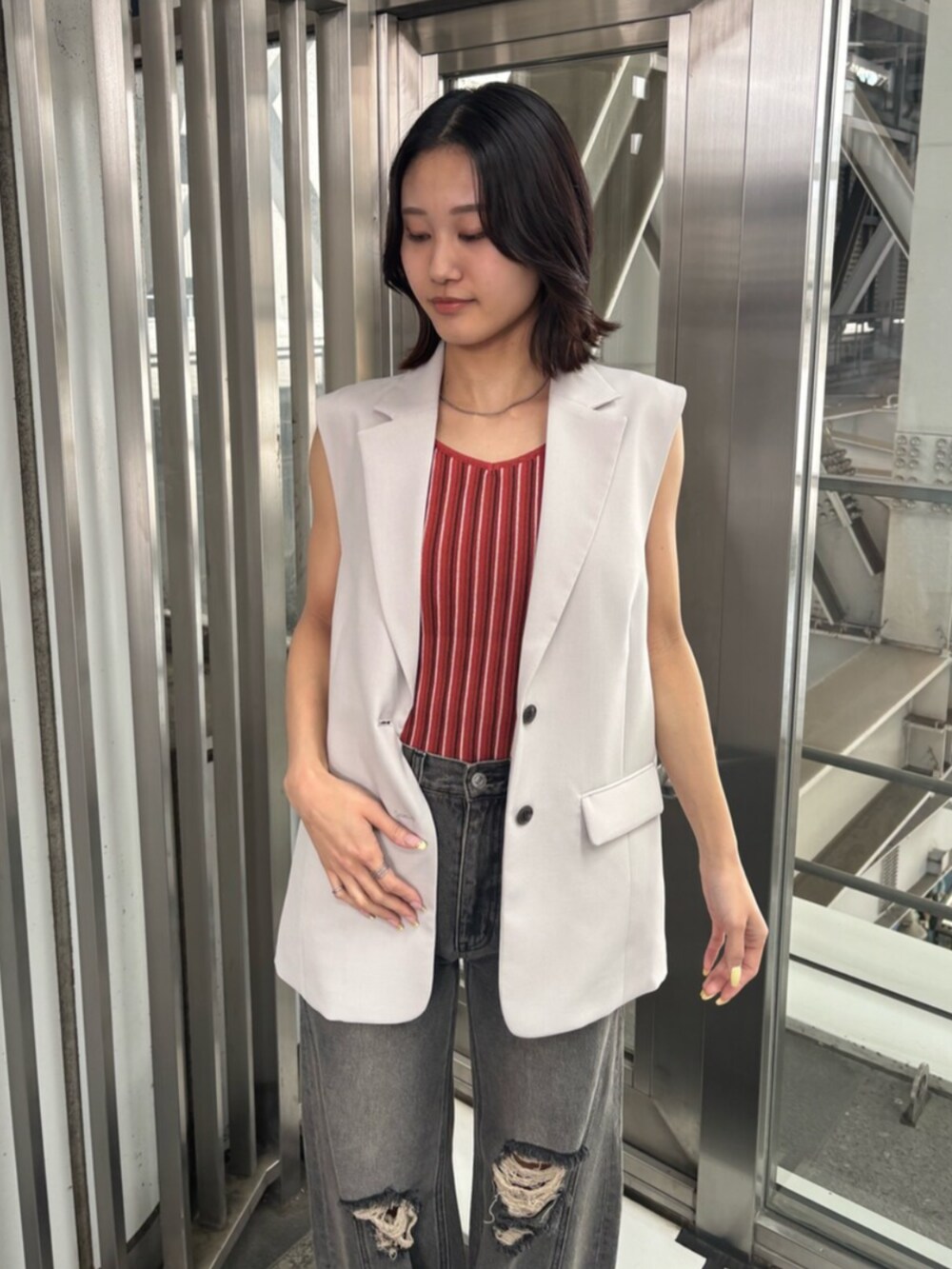 ベージュ系のベスト、オレンジ系のニット/セーター、グレー系のデニムパンツを着用したレディースの春コーディネートの4枚目の写真