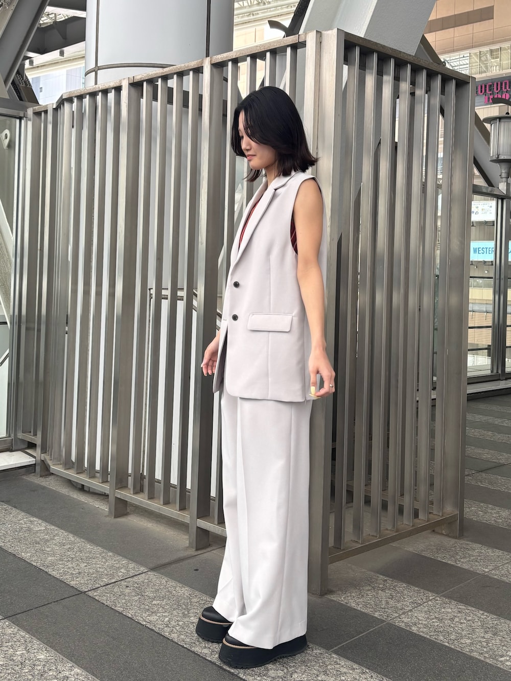 ベージュ系のスラックス、ベージュ系のベスト、オレンジ系のニット/セーターを着用したレディースの春コーディネートの2枚目の写真