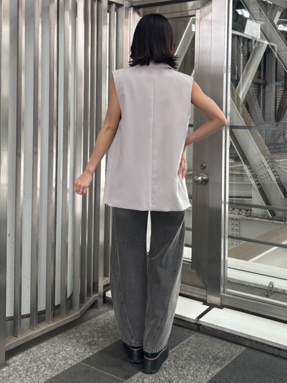 ベージュ系のベスト、オレンジ系のニット/セーター、グレー系のデニムパンツを着用したレディースの春コーディネートの3枚目の写真