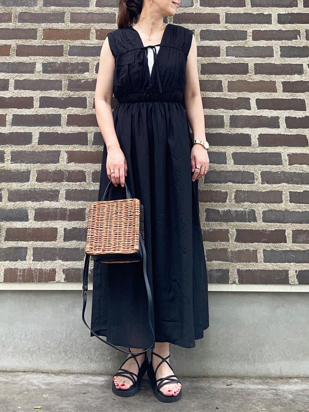 ブラック系のワンピース、ブラック系のサンダル、ブラウン系のかごバッグを着用したレディースの夏コーディネートの5枚目の写真