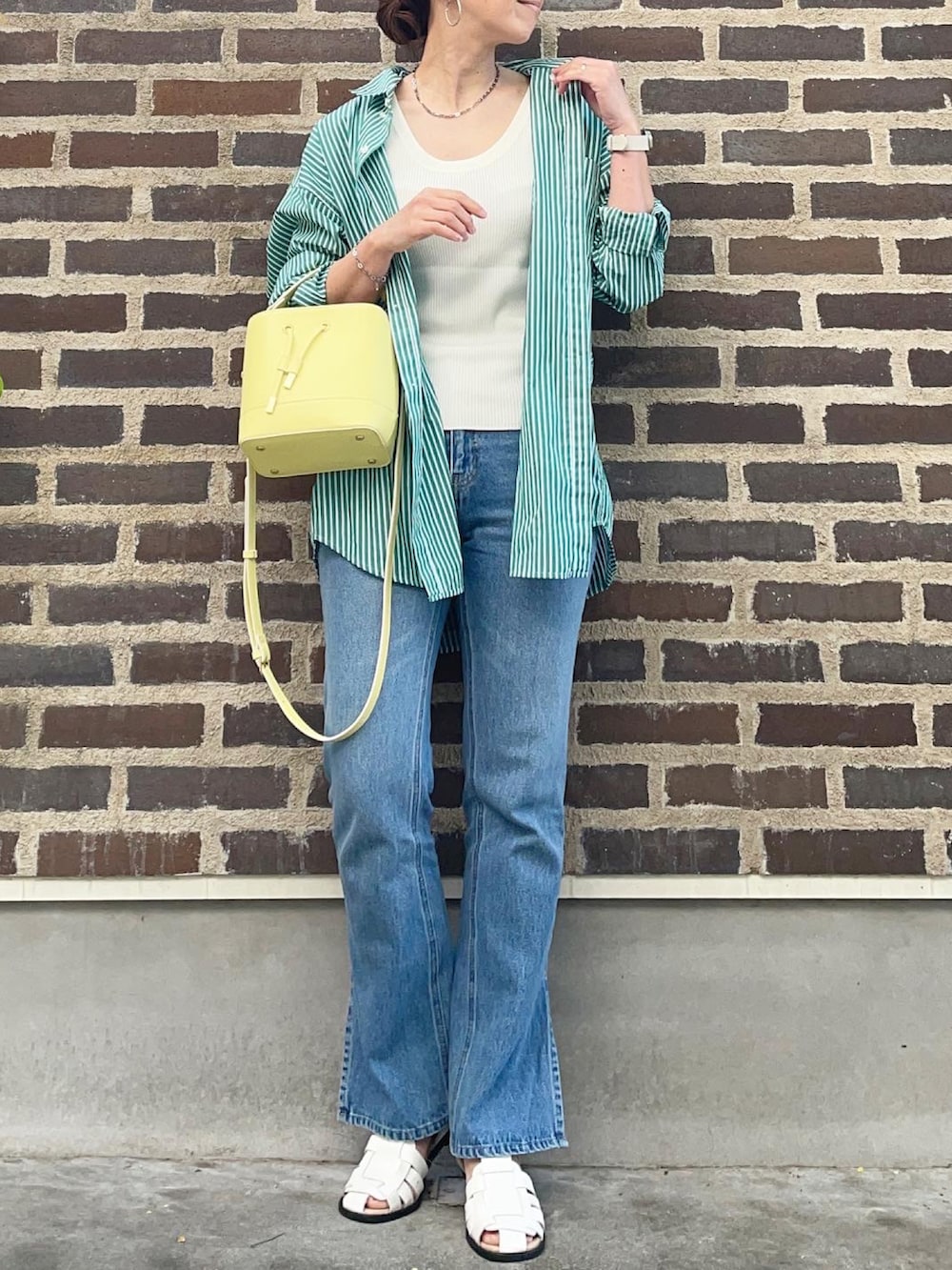 イエロー系のショルダーバッグ、ホワイト系のサンダル、ブルー系のデニムパンツを着用したレディースの春コーディネートの2枚目の写真
