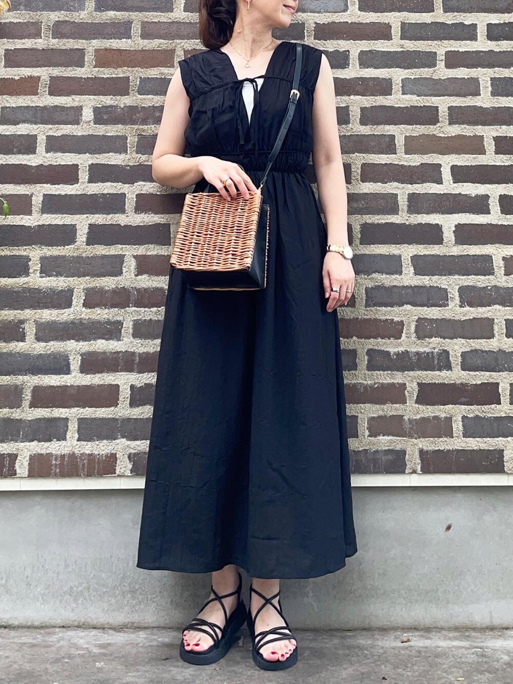 ブラック系のワンピース、ブラック系のサンダル、ブラウン系のかごバッグを着用したレディースの夏コーディネートの4枚目の写真