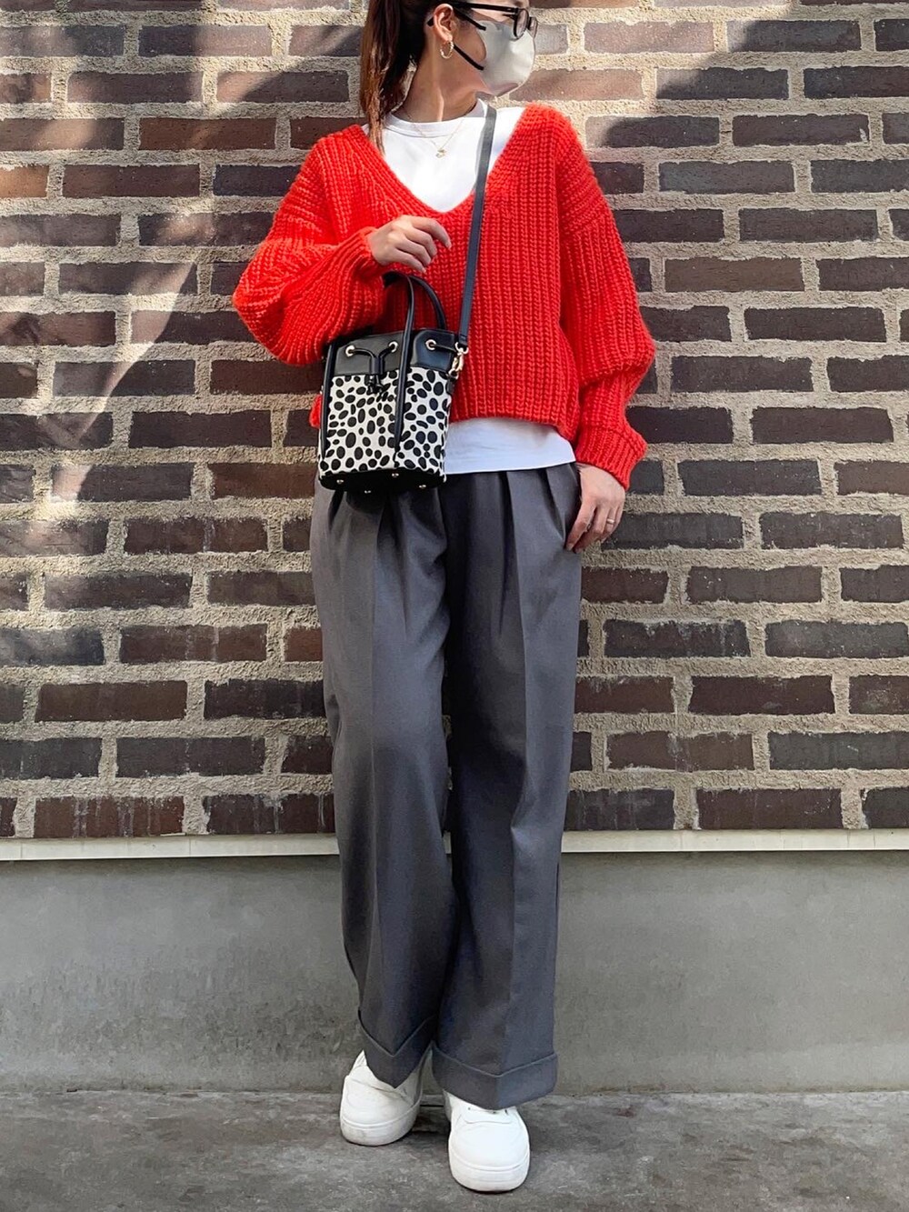 オレンジ系のニット/セーター、グレー系のスラックス、ホワイト系のスニーカーを着用したレディースの秋コーディネートの2枚目の写真