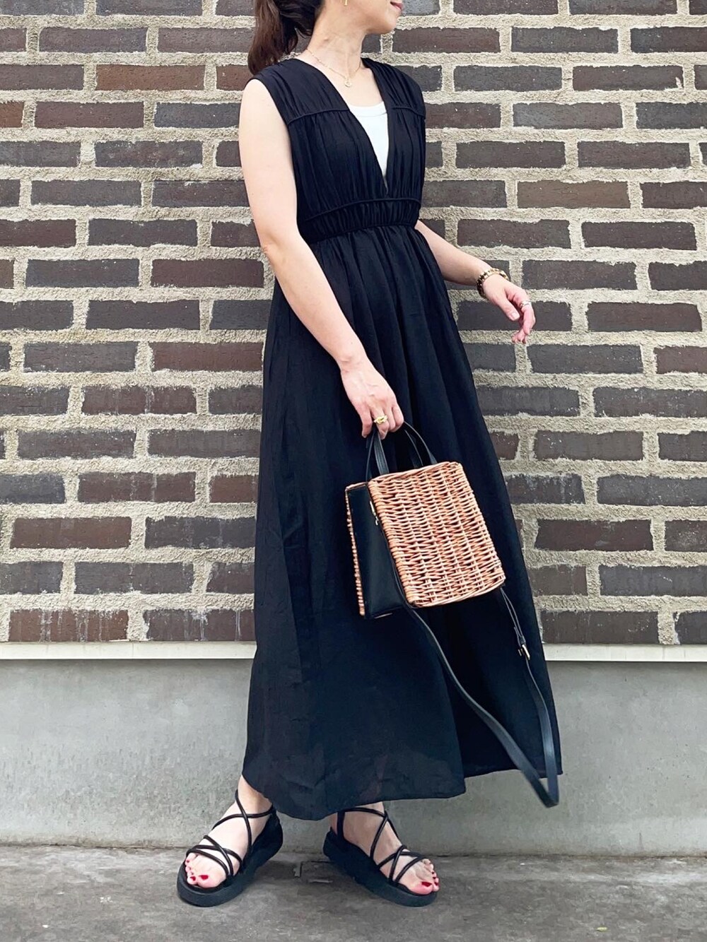 ブラック系のワンピース、ブラック系のサンダル、ブラウン系のかごバッグを着用したレディースの夏コーディネートの3枚目の写真