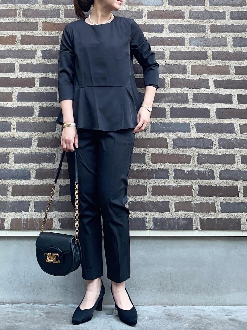 ブラック系のスーツセット、ブラック系のショルダーバッグ、ゴールド系のネックレスを着用したレディースの春コーディネートの5枚目の写真