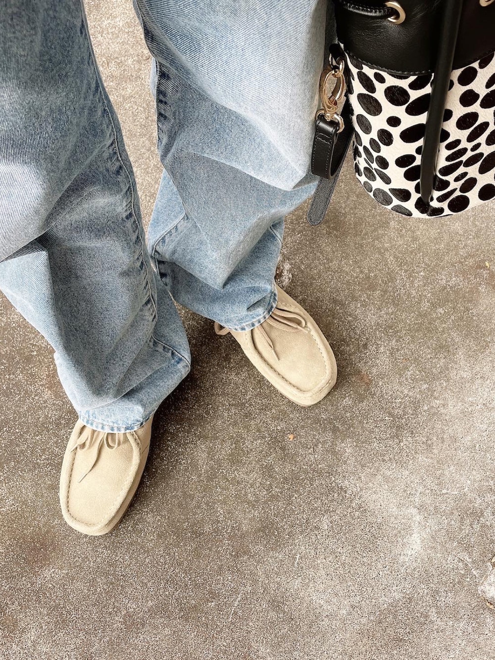 ブラック系のショルダーバッグ、ベージュ系のモカシン/デッキシューズ、ブルー系のデニムパンツを着用したレディースの秋コーディネートの5枚目の写真